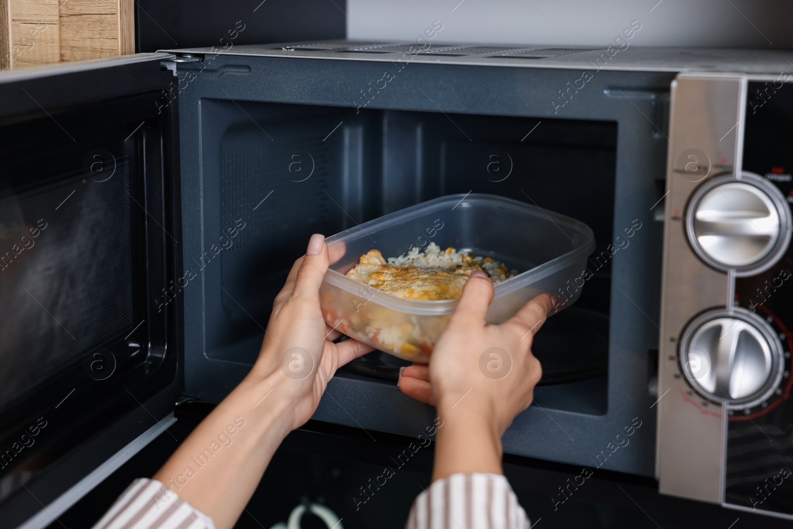 Photo of Woman putting container with lunch into microwave indoors, closeup