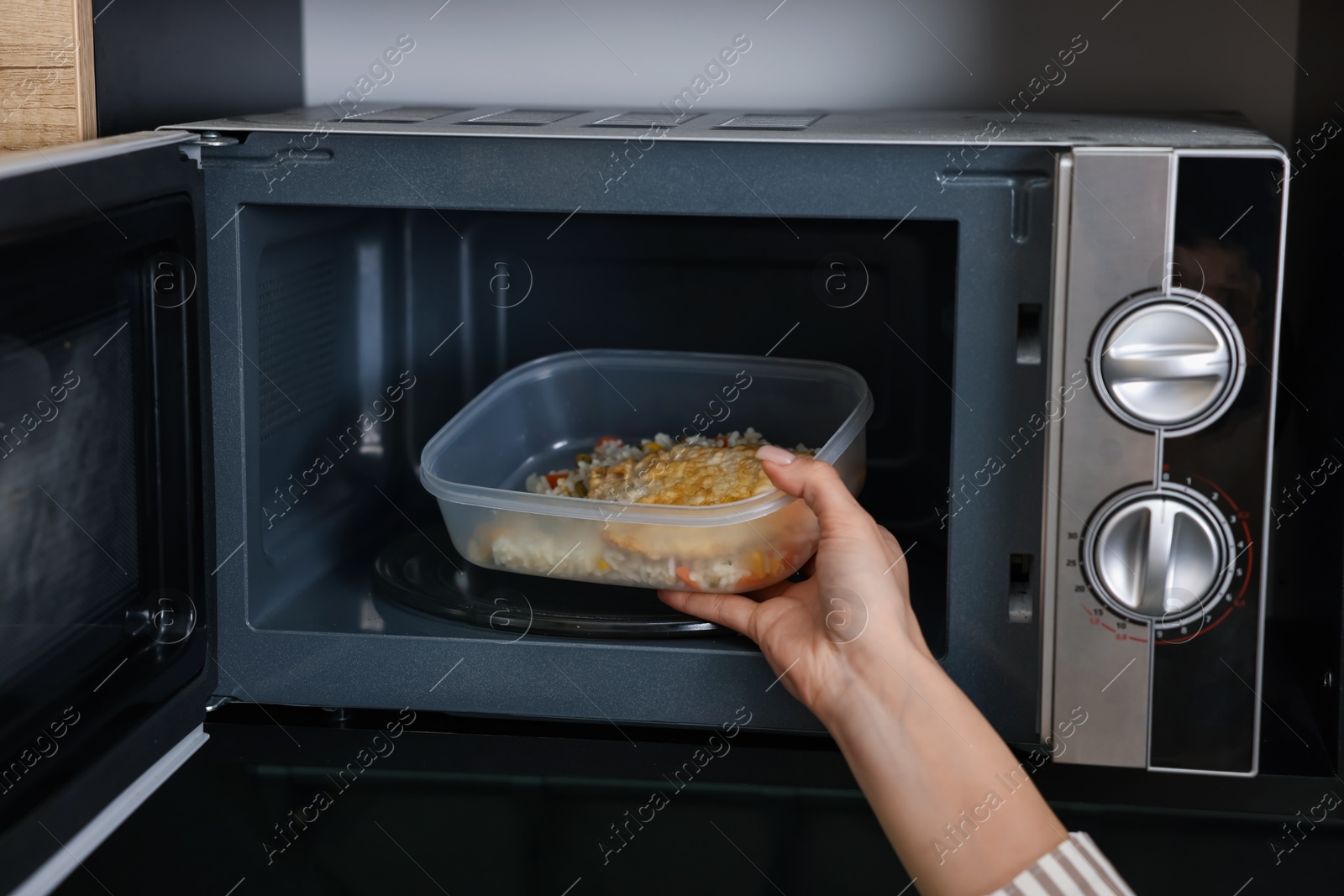 Photo of Woman putting container with lunch into microwave indoors, closeup