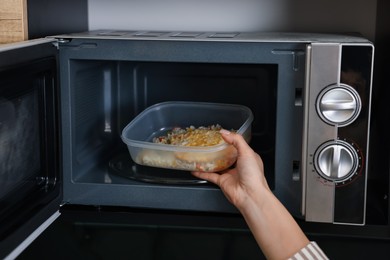 Woman putting container with lunch into microwave indoors, closeup