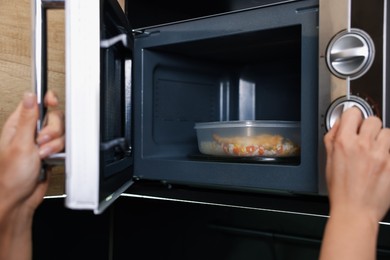 Photo of Woman putting container with lunch into microwave indoors, closeup