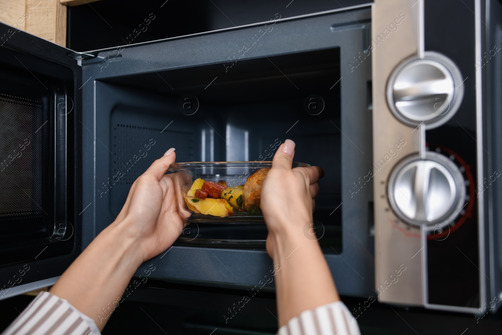 Photo of Woman putting container with lunch into microwave indoors, closeup