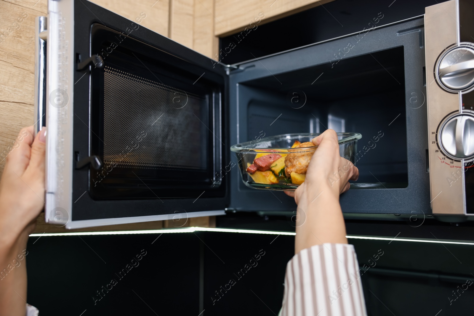 Photo of Woman putting container with lunch into microwave indoors, closeup