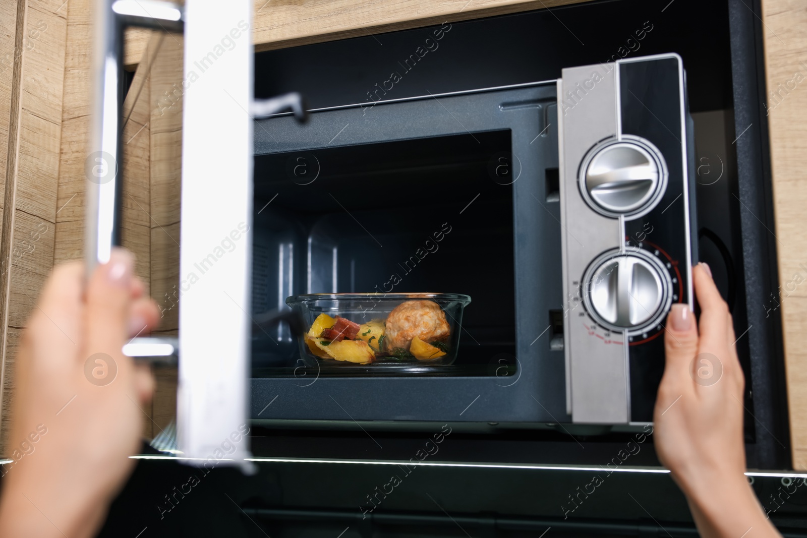 Photo of Woman putting container with lunch into microwave indoors, closeup