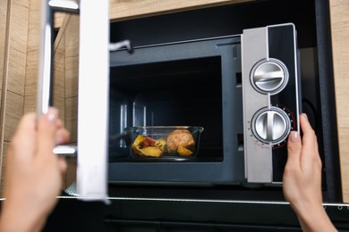 Woman putting container with lunch into microwave indoors, closeup