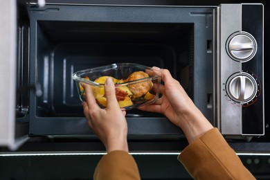 Woman putting container with lunch into microwave indoors, closeup