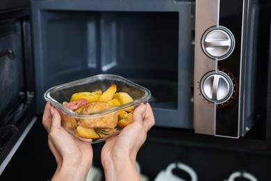 Photo of Woman putting container with lunch into microwave indoors, closeup