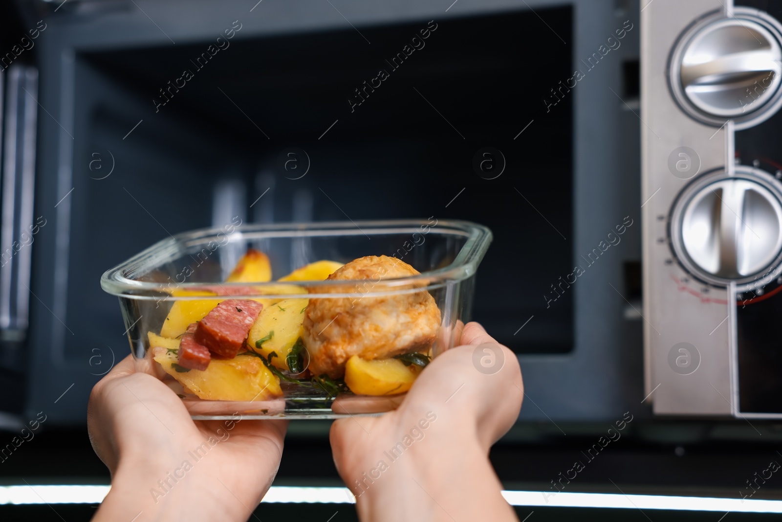 Photo of Woman putting container with lunch into microwave indoors, closeup