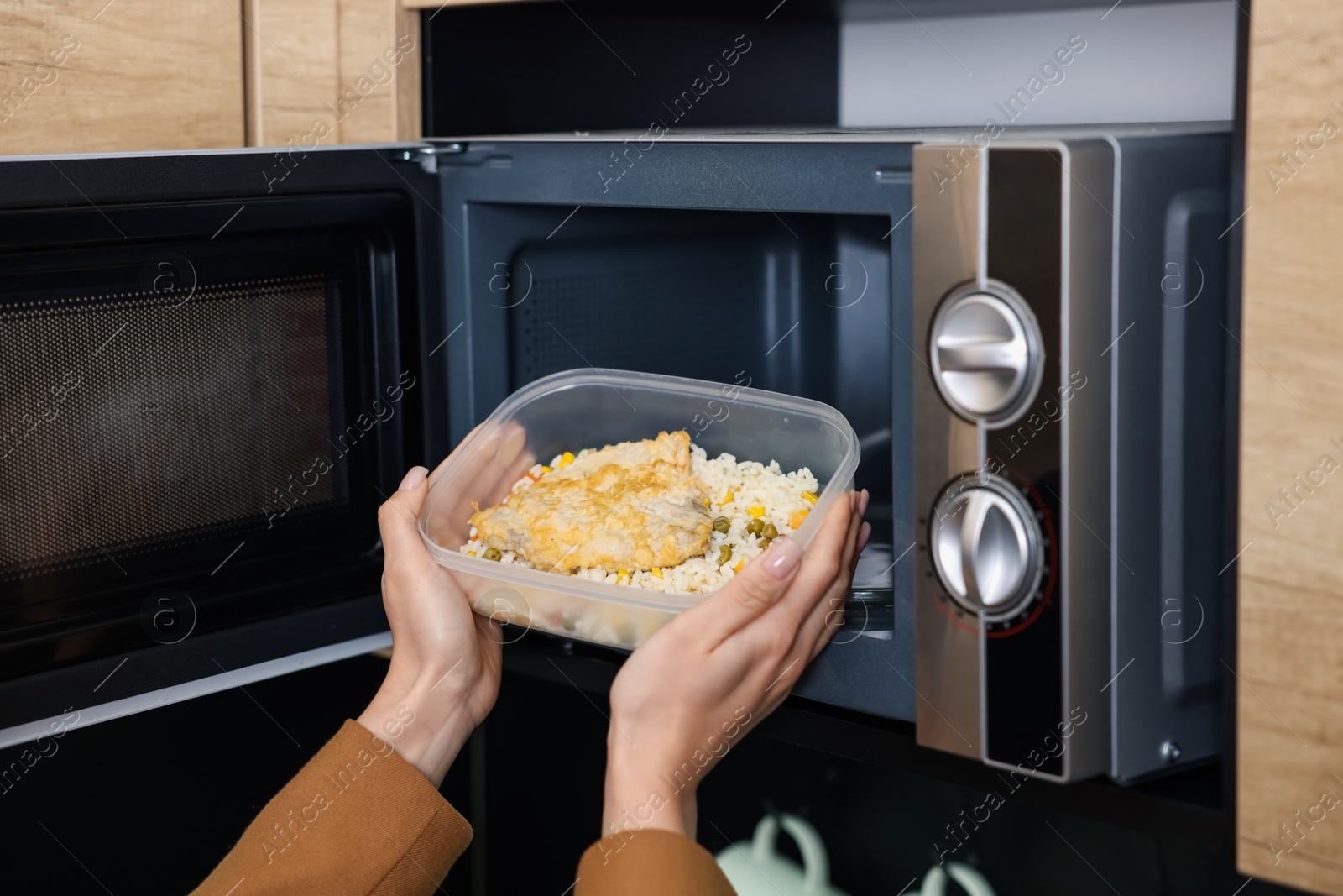 Photo of Woman putting container with lunch into microwave indoors, closeup