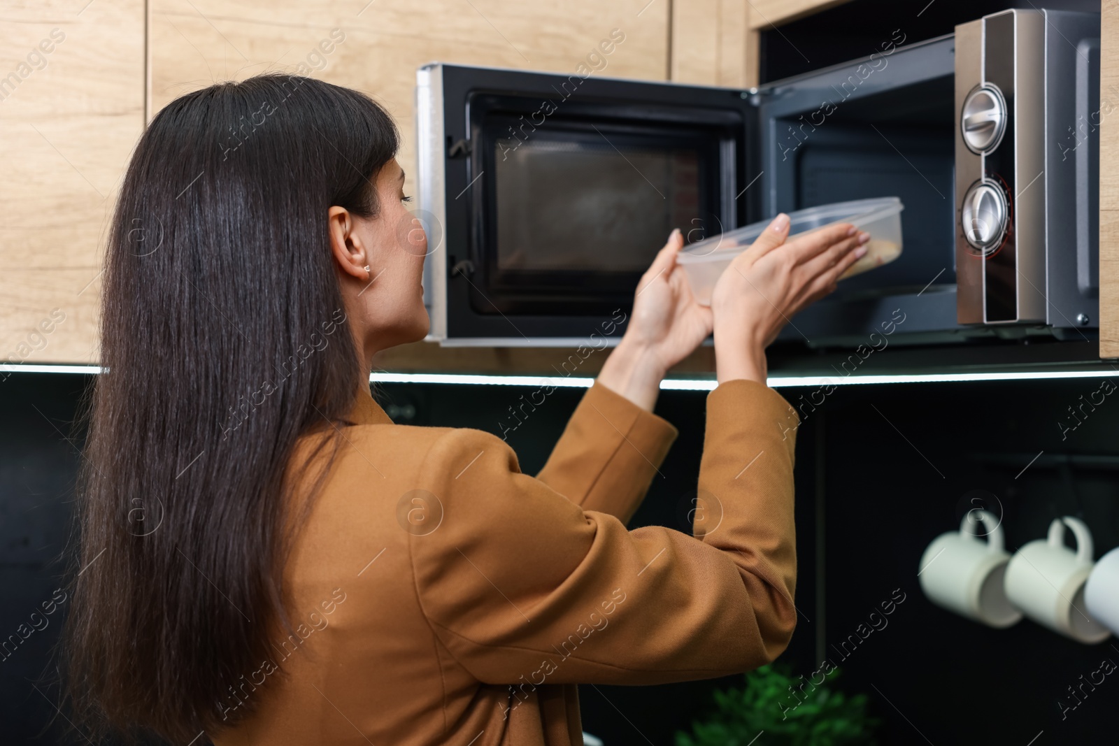 Photo of Woman putting container with lunch into microwave indoors