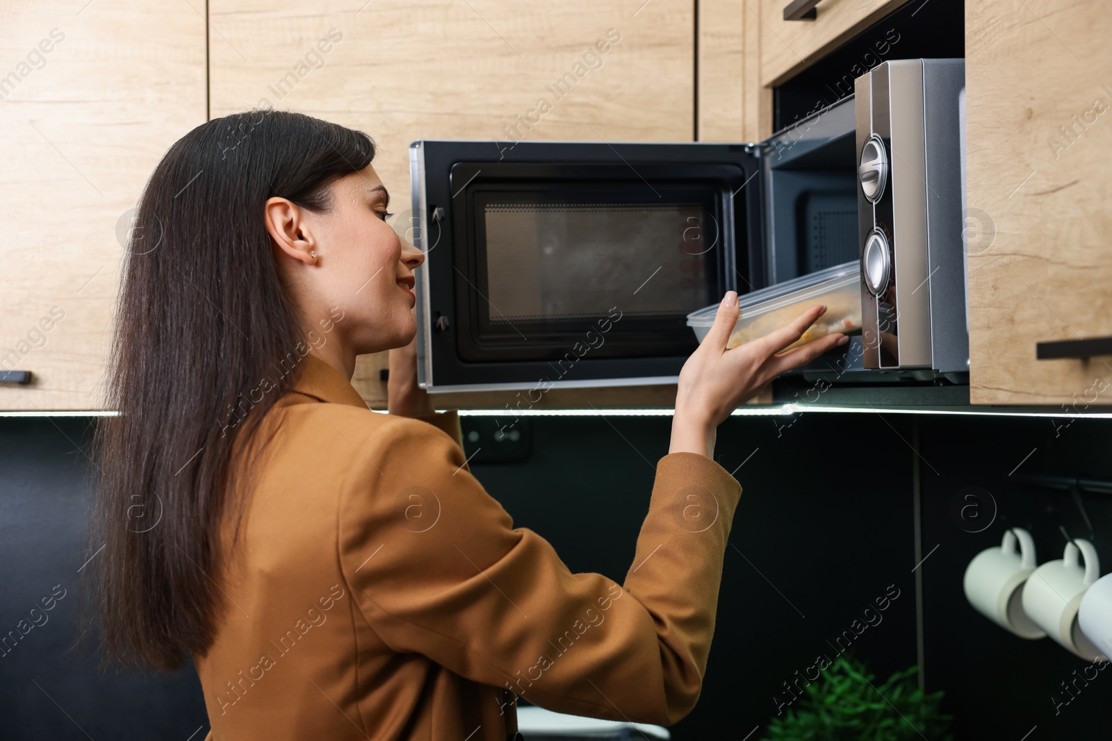 Photo of Woman putting container with lunch into microwave indoors