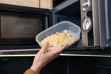 Woman putting container with lunch into microwave indoors, closeup