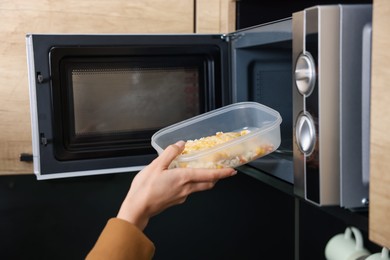 Photo of Woman putting container with lunch into microwave indoors, closeup