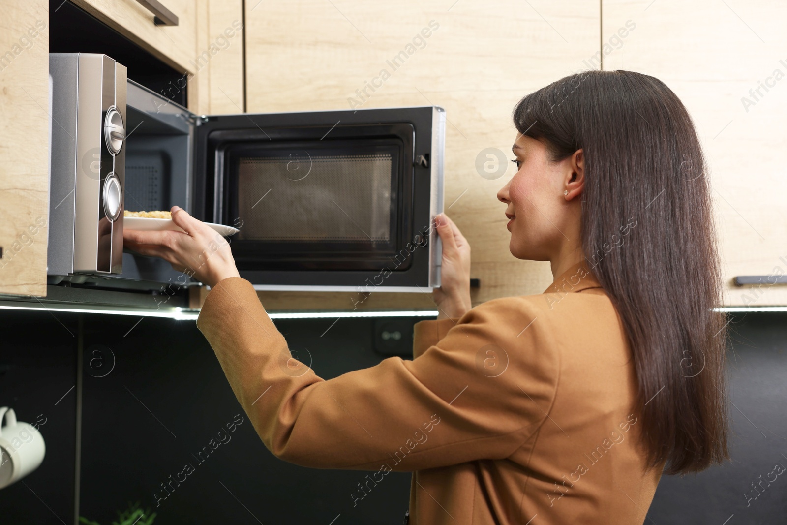 Photo of Woman putting plate with lunch into microwave indoors