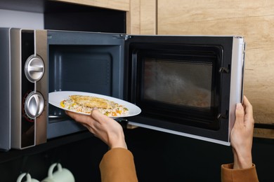 Woman putting plate with lunch into microwave indoors, closeup