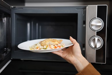 Woman putting plate with lunch into microwave indoors, closeup