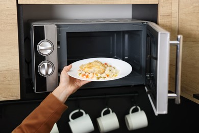 Woman putting plate with lunch into microwave indoors, closeup