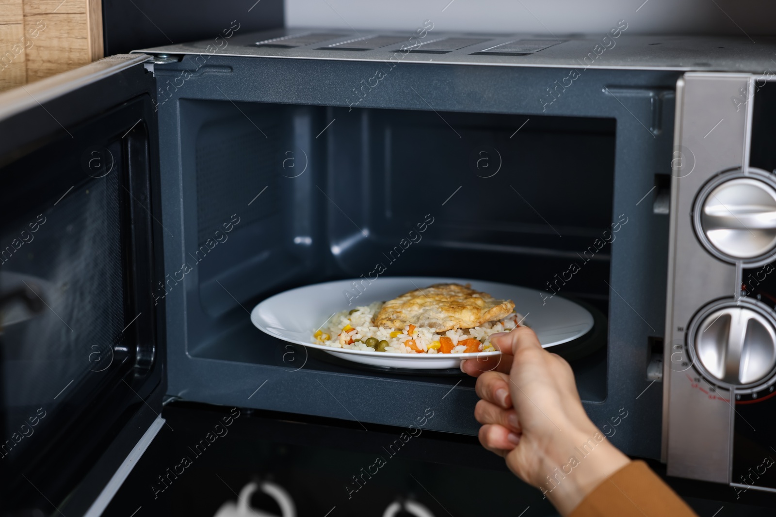 Photo of Woman putting plate with lunch into microwave indoors, closeup