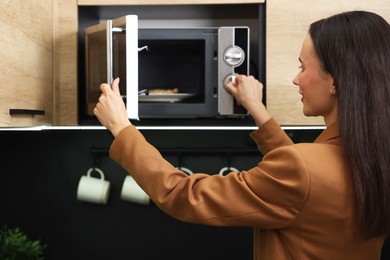 Woman putting plate with lunch into microwave indoors