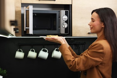 Photo of Woman putting plate with lunch into microwave indoors