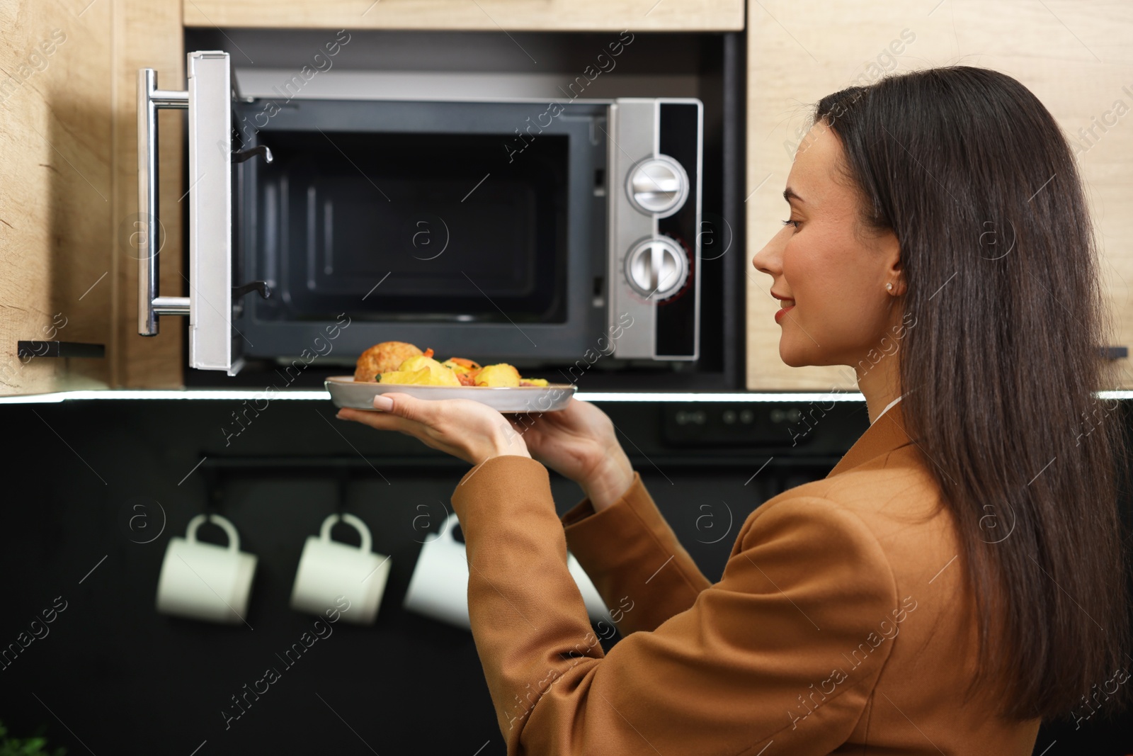 Photo of Woman putting plate with lunch into microwave indoors