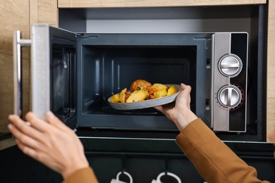 Woman putting plate with lunch into microwave indoors, closeup