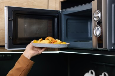 Woman putting plate with lunch into microwave indoors, closeup