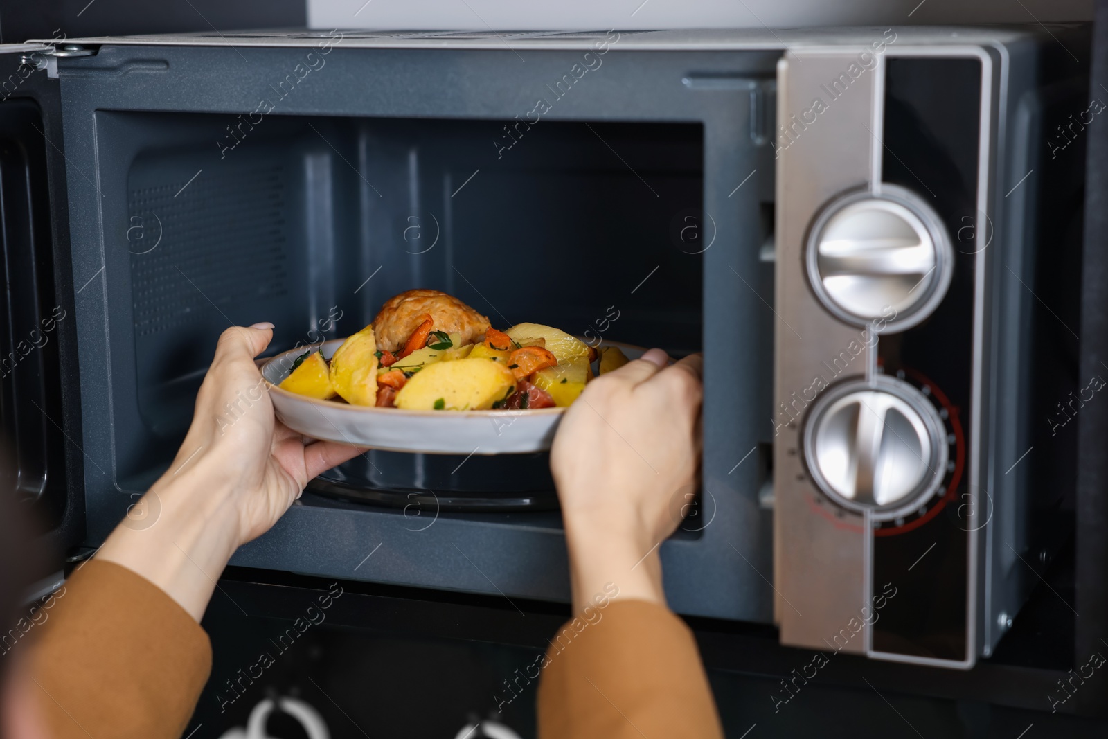 Photo of Woman putting plate with lunch into microwave indoors, closeup