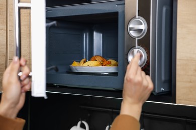 Woman putting plate with lunch into microwave indoors, closeup