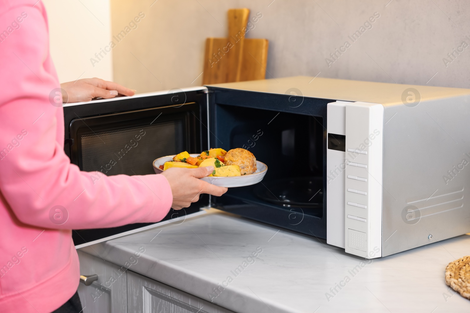 Photo of Woman putting plate with lunch into microwave indoors, closeup