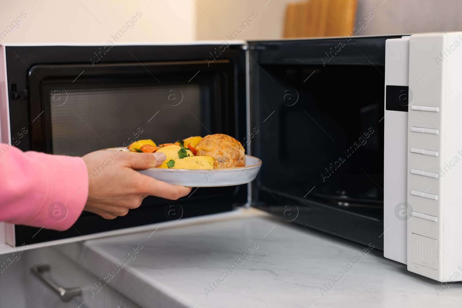 Photo of Woman putting plate with lunch into microwave indoors, closeup