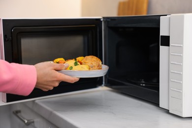 Woman putting plate with lunch into microwave indoors, closeup