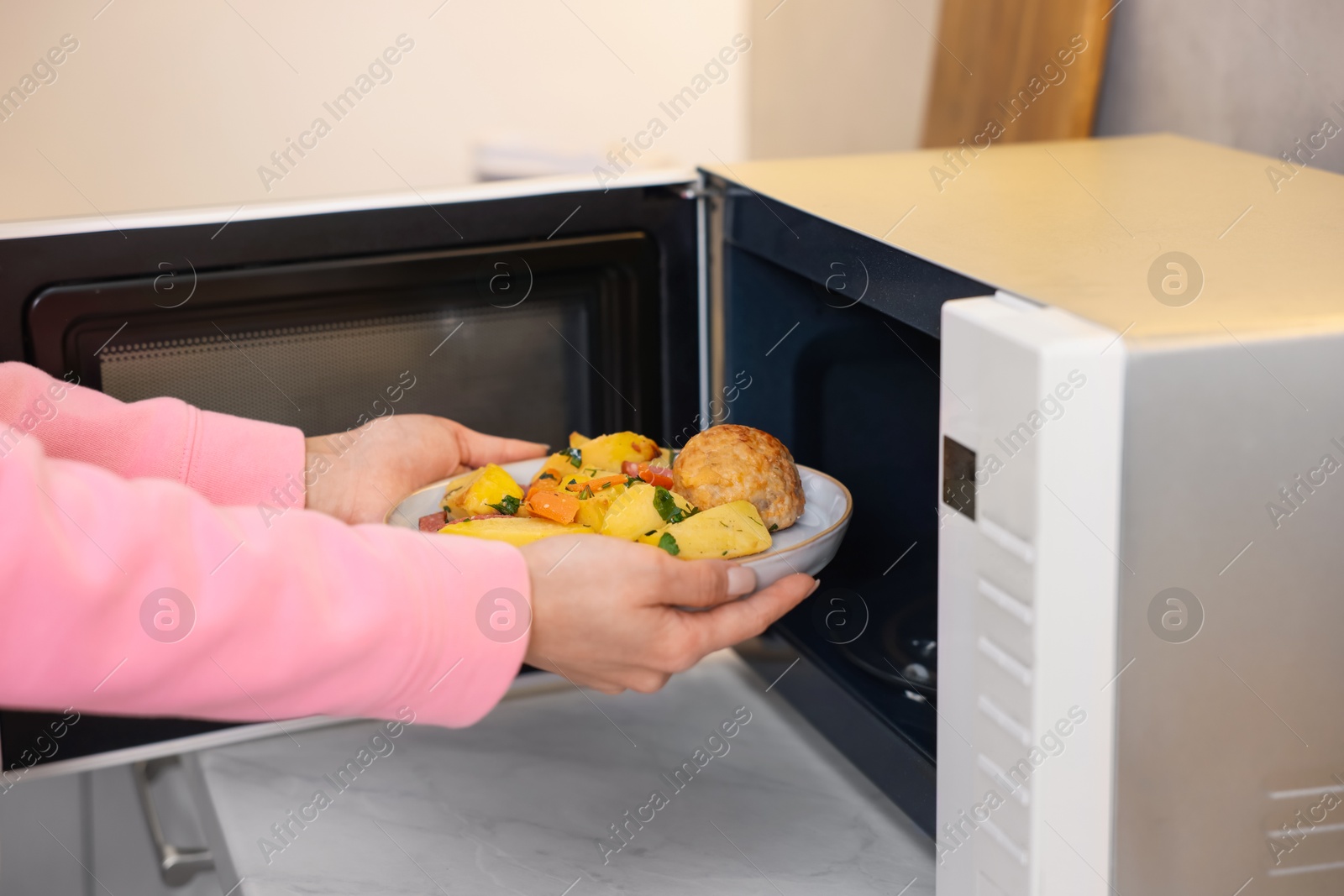 Photo of Woman putting plate with lunch into microwave indoors, closeup