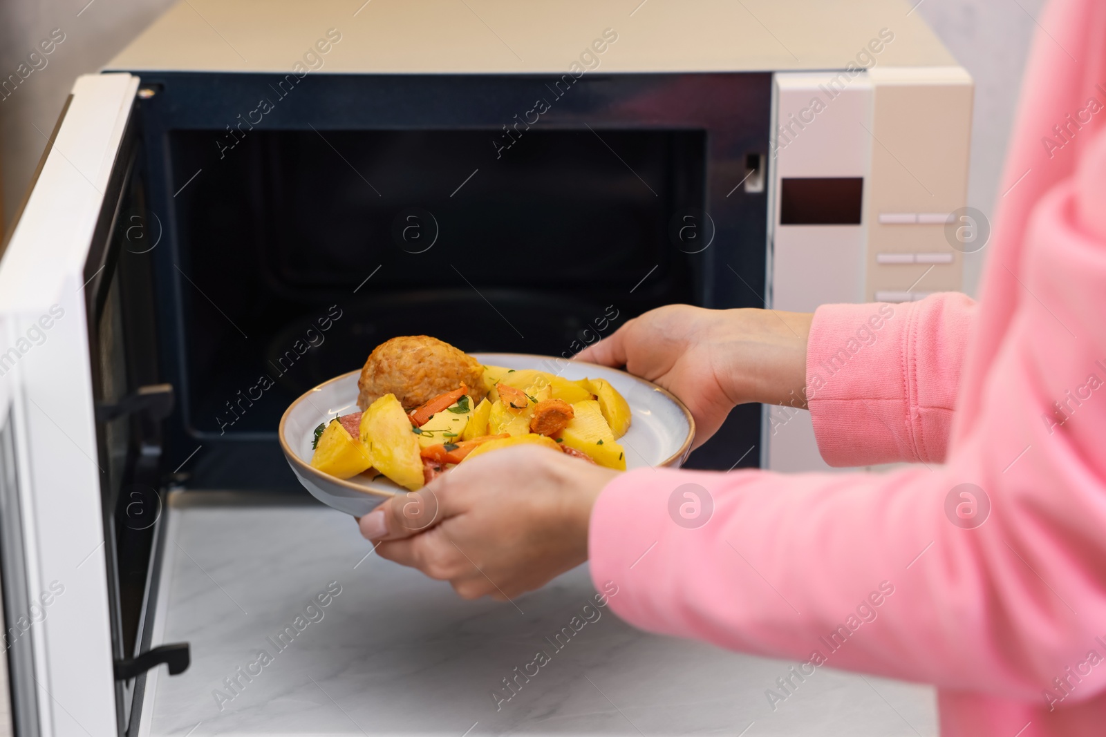 Photo of Woman putting plate with lunch into microwave indoors, closeup