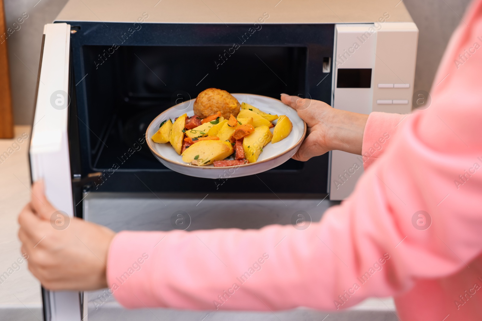 Photo of Woman putting plate with lunch into microwave indoors, closeup