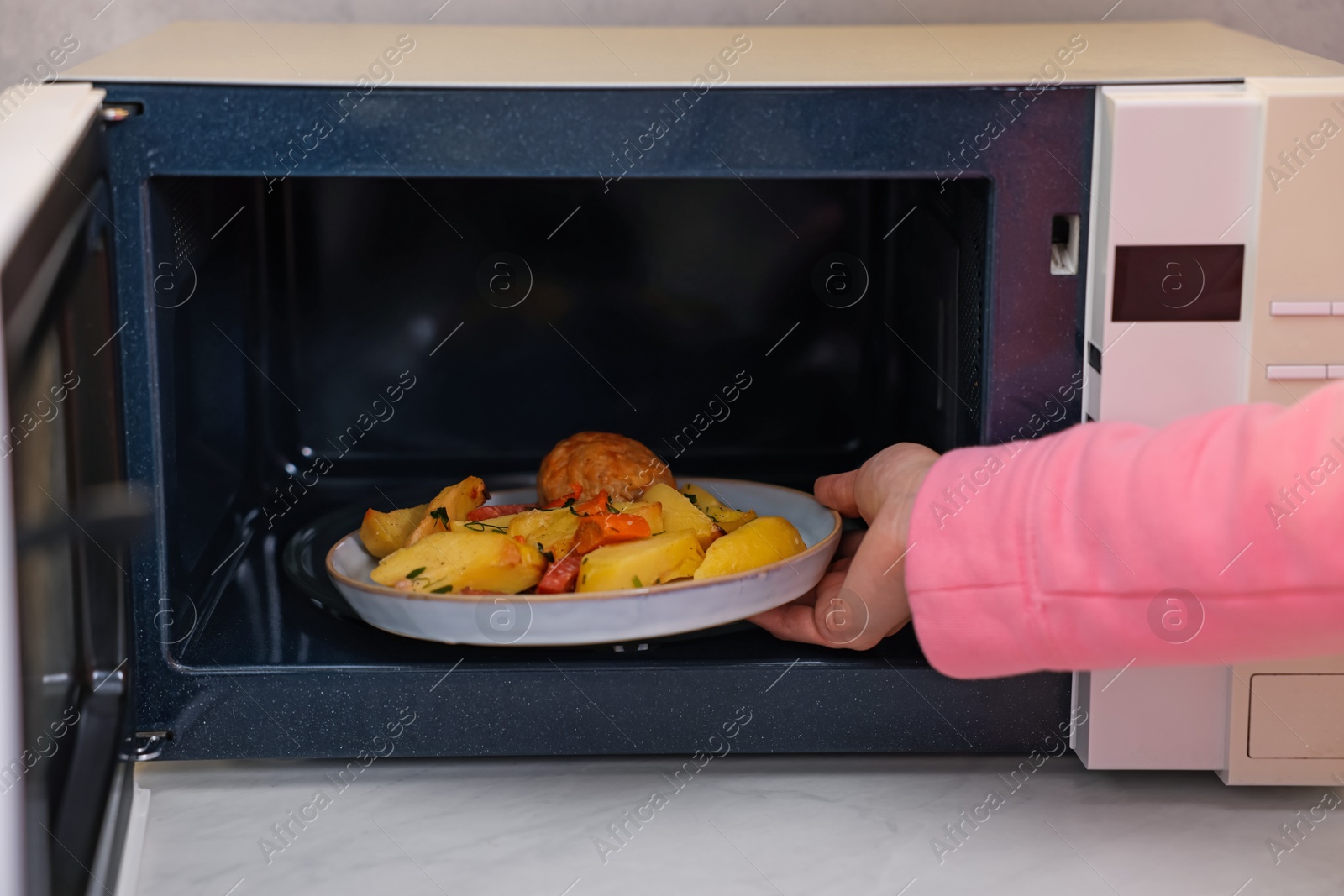 Photo of Woman putting plate with lunch into microwave indoors, closeup