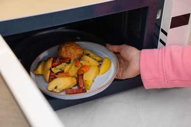 Woman putting plate with lunch into microwave indoors, closeup