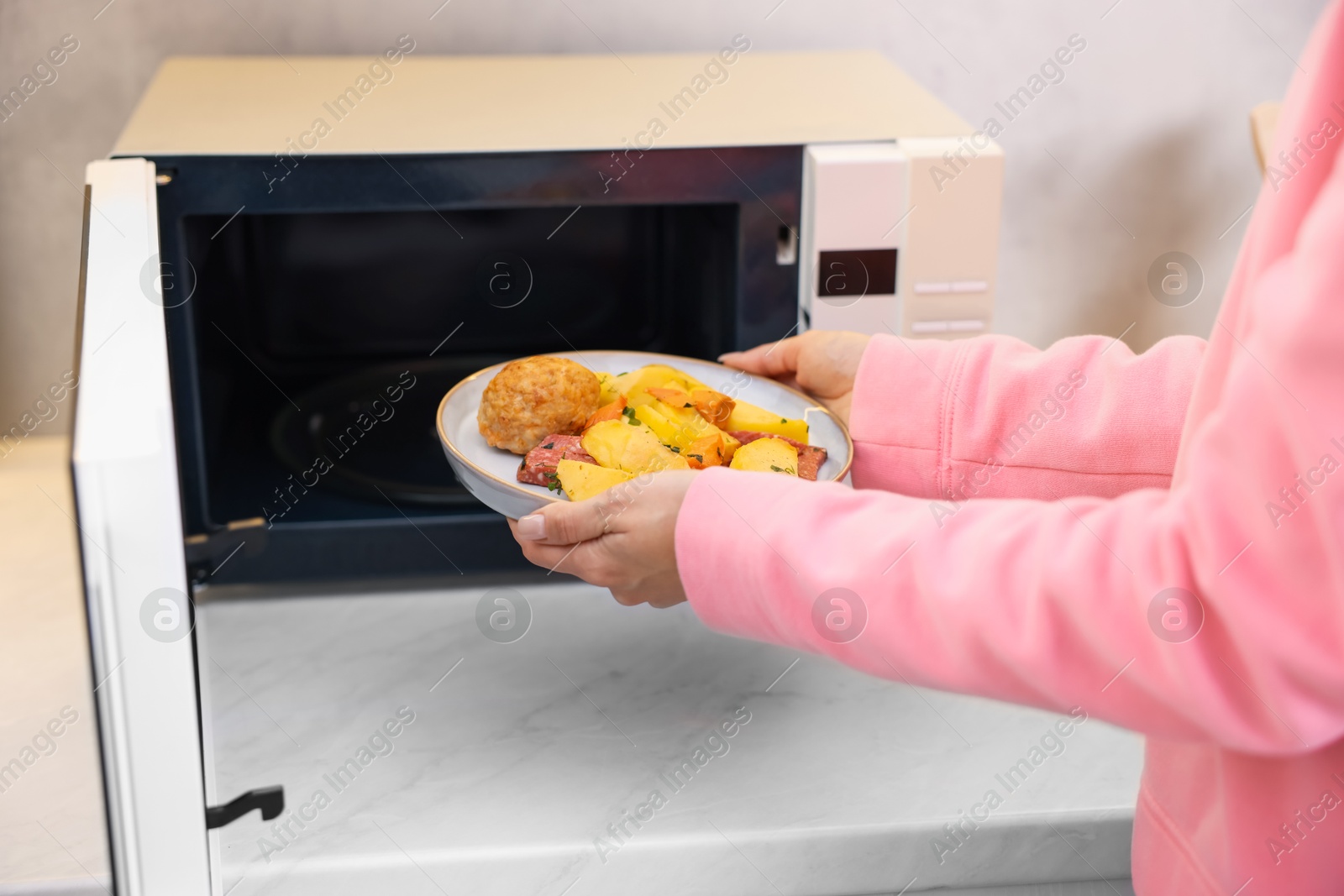 Photo of Woman putting plate with lunch into microwave indoors, closeup