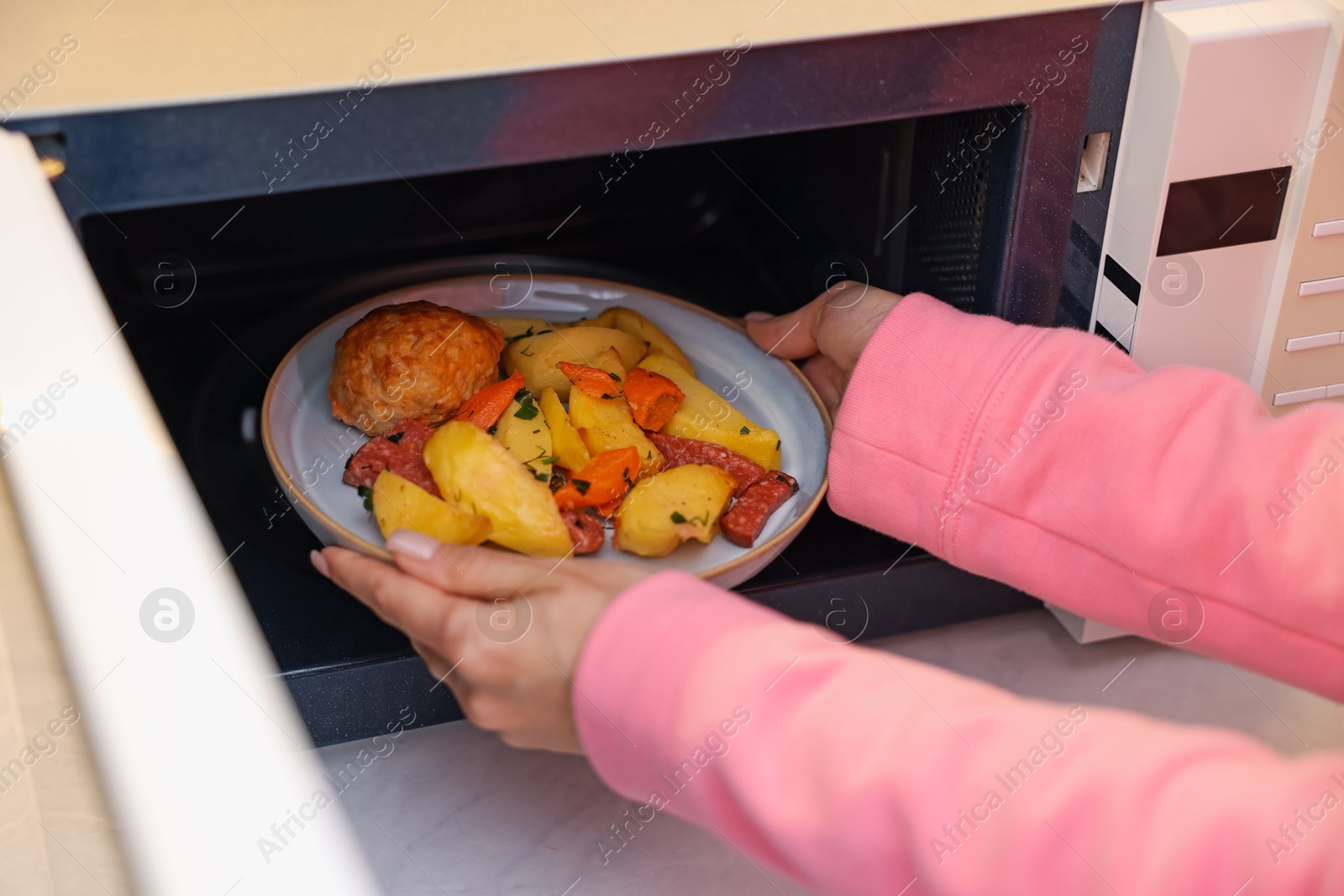 Photo of Woman putting plate with lunch into microwave indoors, closeup