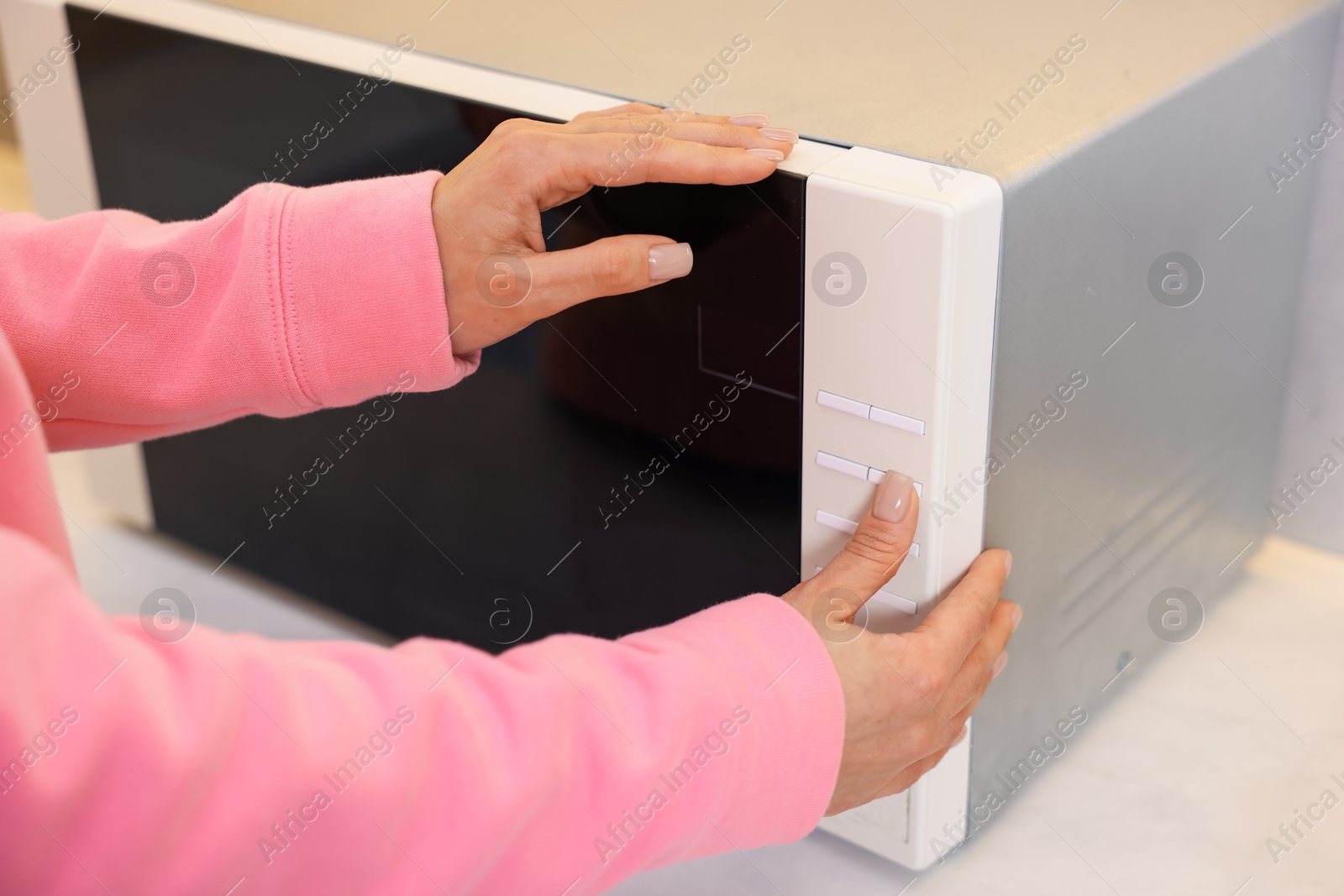 Photo of Woman turning on microwave at home, closeup