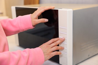 Photo of Woman turning on microwave at home, closeup