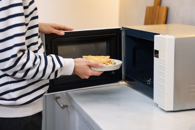 Woman putting plate with lunch into microwave indoors, closeup