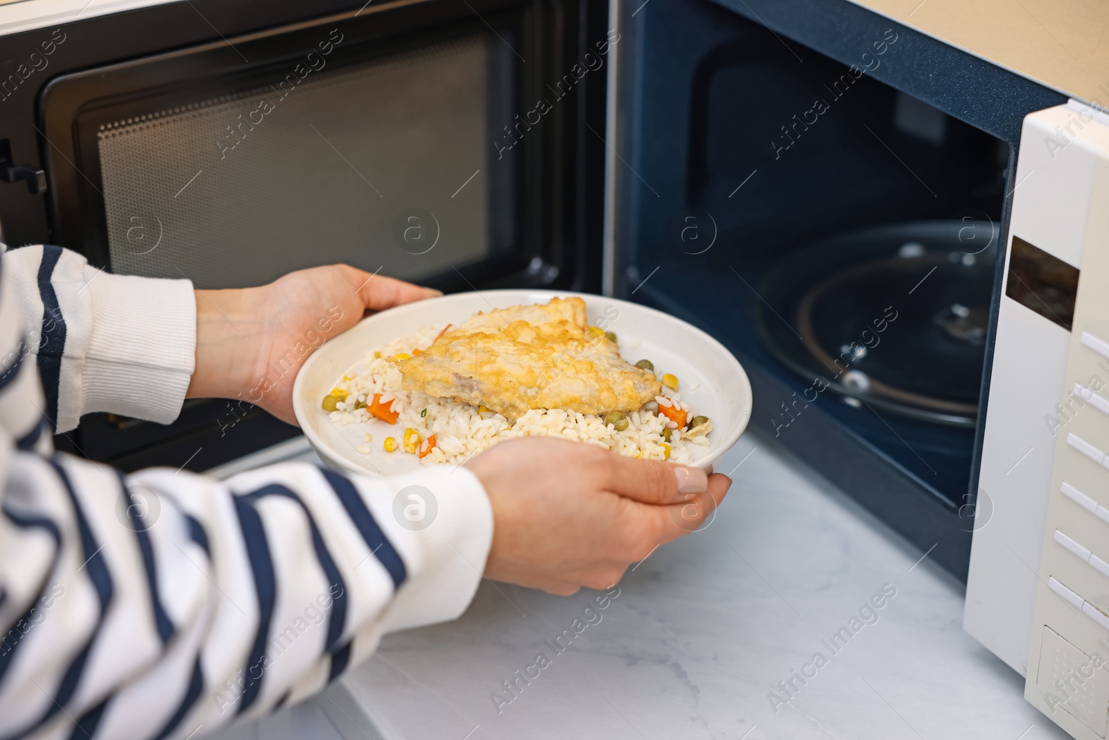 Photo of Woman putting plate with lunch into microwave indoors, closeup