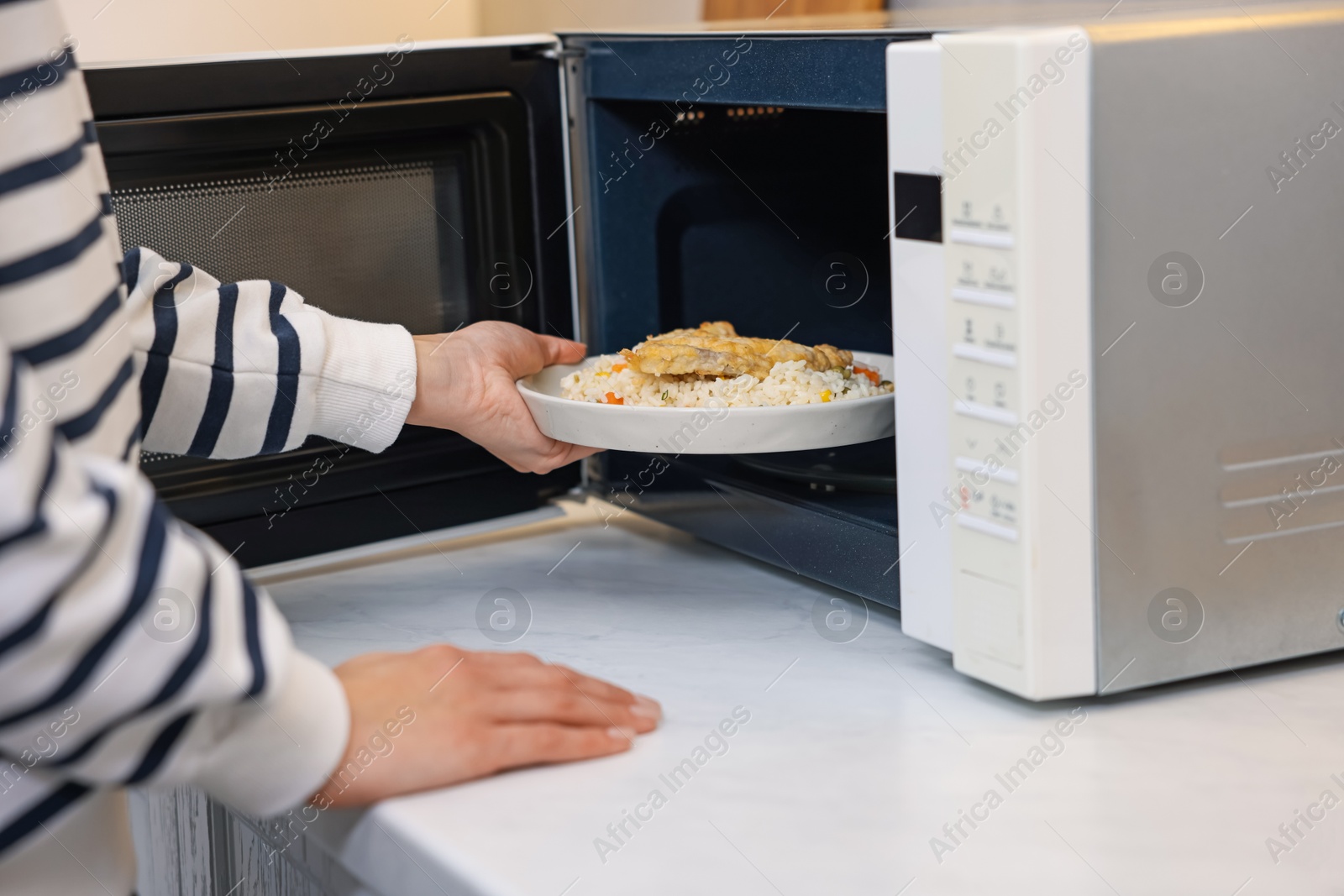 Photo of Woman putting plate with lunch into microwave indoors, closeup