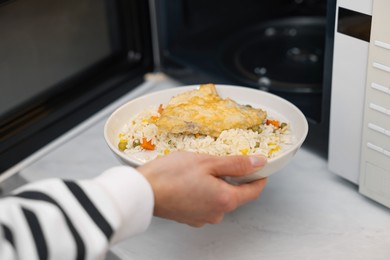 Woman putting plate with lunch into microwave indoors, closeup