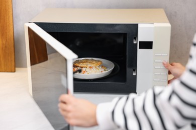 Woman putting plate with lunch into microwave indoors, closeup