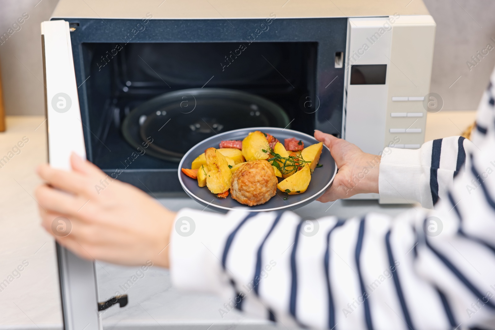 Photo of Woman putting plate with lunch into microwave indoors, closeup