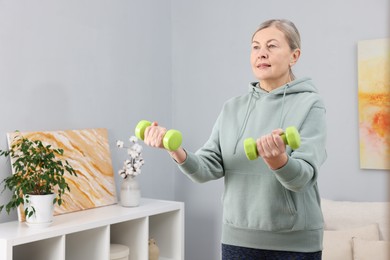 Elderly woman exercising with dumbbells at home