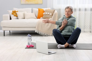 Elderly woman exercising near laptop at home