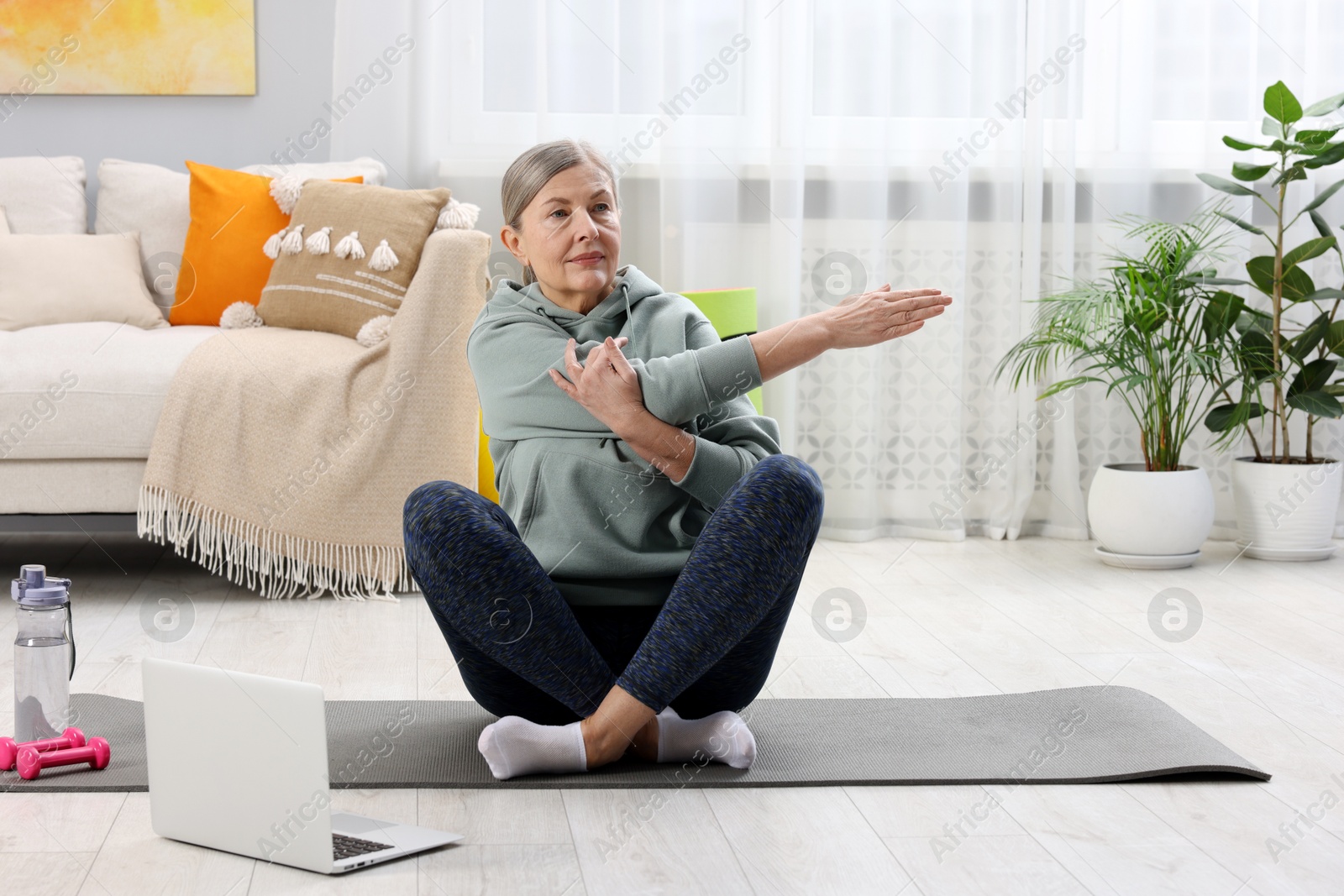 Photo of Elderly woman exercising near laptop at home