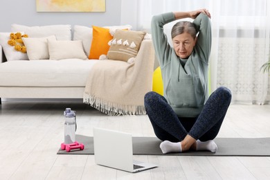 Elderly woman exercising near laptop at home